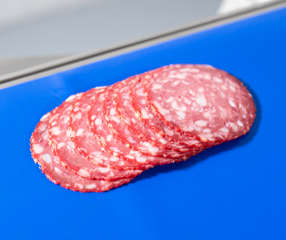 Rebanadas finas de embutido tipo salami colocadas sobre una cinta transportadora azul